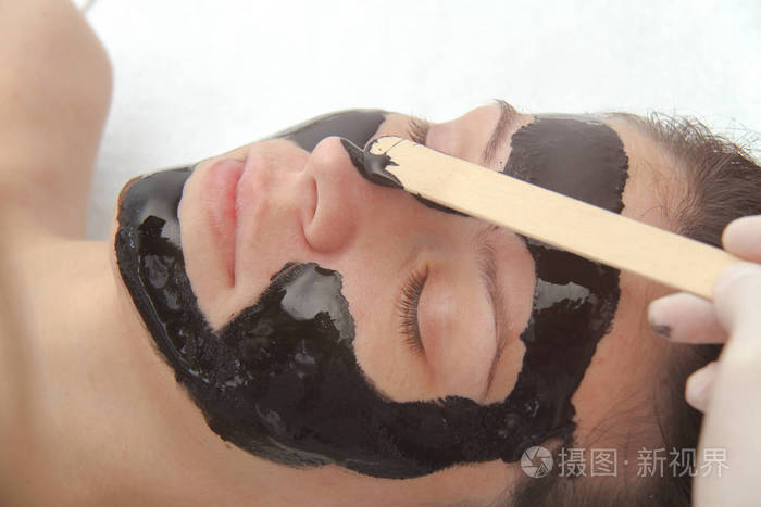 Young beautiful woman applying black charcoal facial mask. Skin 