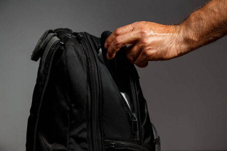 小偷的手从灰色背景的背包里掏出一个钱包照片