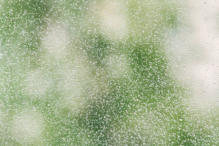 雨滴落在背景多云的窗玻璃表面。在多云背景下孤立的雨滴的自然模式。