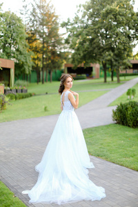 高加索美丽的新娘站在花园里，穿着白色长裙。