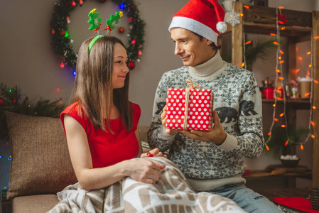 年轻的妻子给丈夫一个惊喜的礼盒。一对已婚夫妇在家里庆祝圣诞节和新年