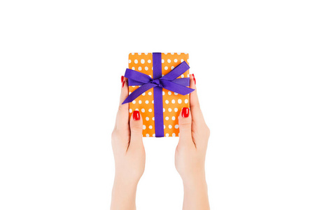 女人用手给圣诞节或其他节日手工制作的橙色纸和紫色丝带礼物。白色背景，顶视图。感恩节礼品盒概念
