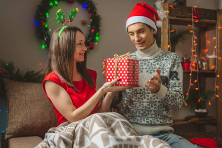 年轻的妻子给丈夫一个惊喜的礼盒。一对已婚夫妇在家里庆祝圣诞节和新年