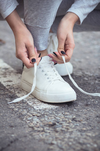 女孩蹲下来系鞋带的白色运动鞋在柏油路上,秋天的运动概念户外照片