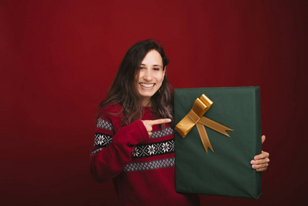 穿着红色毛衣的快乐年轻女子指着绿色的圣诞大礼盒