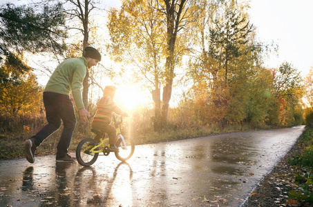 Father teaches his little child to ride bike in autumn park. Hap