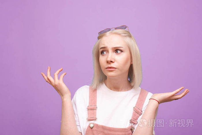 一个迷惑不解的金发女孩的画像穿着可爱的衣服在紫色的背景下斜视着