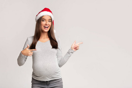 戴圣诞帽的孕妇手指着一边，灰色背景