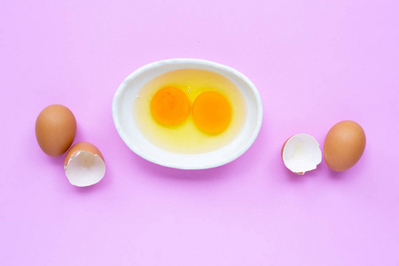 Two egg yolk and white in a bowl on pink background. 