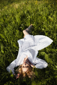 Girl in a long white dress lies on the grass in a field. Blonde 