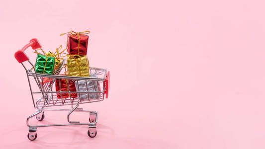 圣诞购物季概念-迷你红色购物车手推车装满礼品盒,隔离在淡粉色背景上