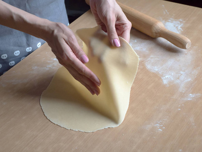 Hands roll out the thin dough. Close up. 