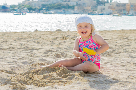 可爱的蹒跚学步的女孩微笑着在白色沙滩上玩耍