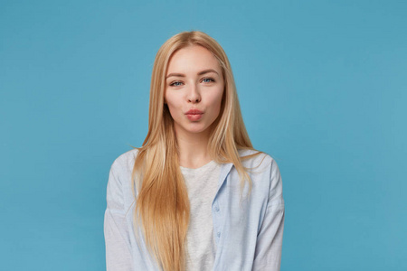 室内拍摄的是一位金发美女,发型随意,穿着蓝色衬衫和灰色t恤,在蓝色