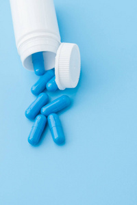 蓝色的胶囊，蓝色背景的药丸。装在白色罐子里的胶囊。维生素，女性健康的营养补充剂