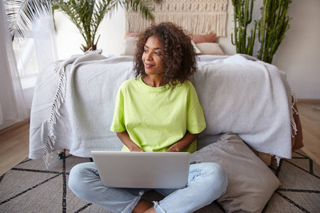 可爱的深色皮肤,棕色卷发的年轻女子在家里摆好姿势,坐在卧室的床前