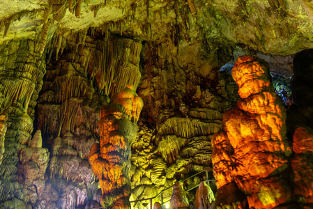 洞穴岩层是在五颜六色的光线下形成的钟乳石和石笋。克里特岛宙斯洞穴黑暗大厅石笋形成的奇迹。度假和旅游概念。水平
