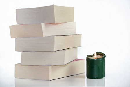 白色背景下的绿色蜡烛和一堆书的构图