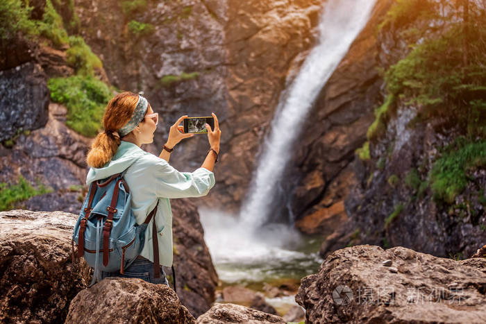 快乐的旅行者女人在丛林中拍摄雄伟的瀑布。徒步旅行和观光概念