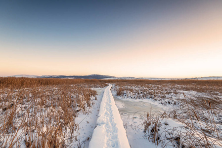 乡村冬季景观。日出在雪路上。