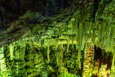 洞穴岩层是在五颜六色的光线下形成的钟乳石和石笋。克里特岛宙斯洞穴黑暗大厅石笋形成的奇迹。度假和旅游概念。水平