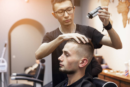 一个帅哥在灰色的墙壁背景上用干凝胶给客户做发型男专业理发师给帅哥