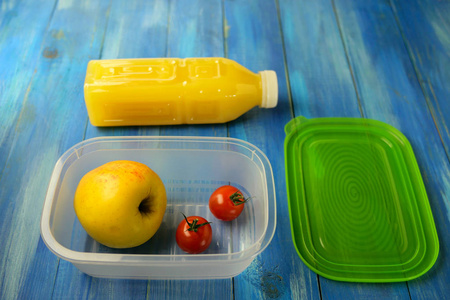 Plastic lunch box with large ripe apple and two cherry tomatoes 