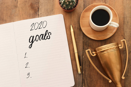 top view 2020目标列表的商业理念，木制桌子上有笔记本咖啡杯和金色奖杯