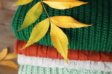 木质背景上的一叠温暖的针织衣服和秋叶，特写