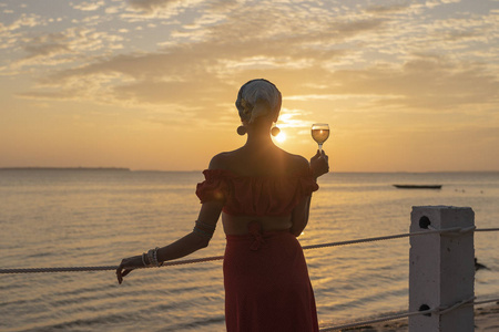 在热带海滩上,女人手拿酒杯,对着美丽的夕阳,近距离拍摄照片