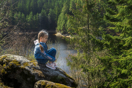 一个女孩坐在悬崖上看着河。河的美丽景色。大自然中的女孩。