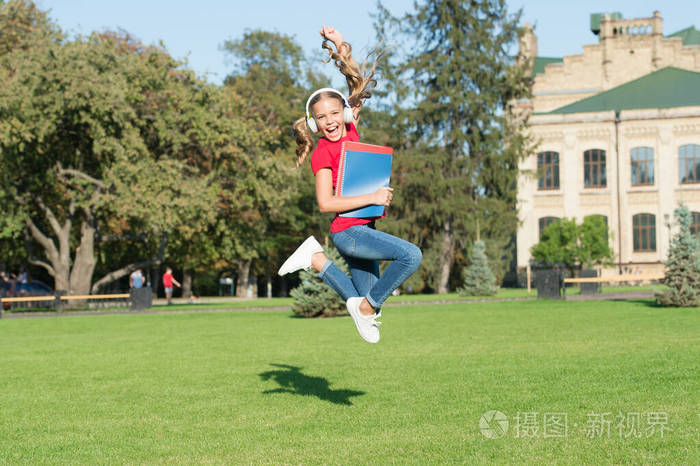 心情愉快地开始上学。快乐的女学生跳到绿草地上听音乐。戴着耳机的活跃的小孩拿着课本。回到学校。学校假期。暑假。小学教育