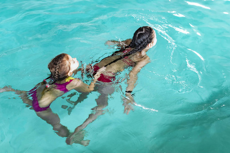 两个女孩在游泳池里游泳。两个姐妹在游泳池里。两个快乐的女孩在游泳池。漂亮女孩们游泳，玩得很开心水。活跃假日。