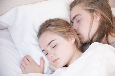 一对年轻夫妇躺在床上拥抱睡觉，躲在毯子后面的特写镜头。年轻家庭和健康睡眠的概念