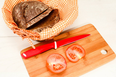 红色番茄专用刀，柳条篮子里的自制面包，餐巾和西红柿，放在白色的木桌上。