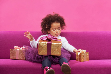 Cute little girl with a lot of gift boxes sitting on sofa 