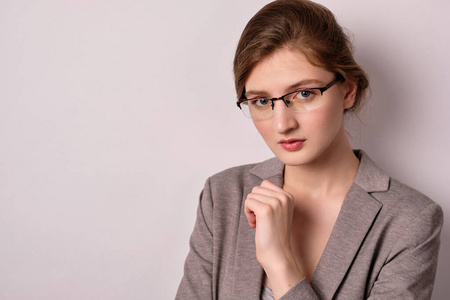 A girl in a gray jacket and glasses stands on a light background