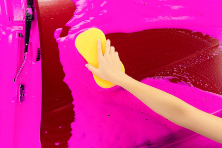 手握黄色海绵在车上，用于清洗粉色泡沫背景。俯视图