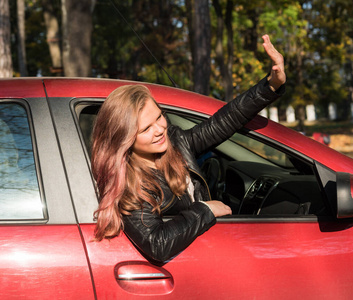 Cute laughing teen girl hanging out her head from a car through 