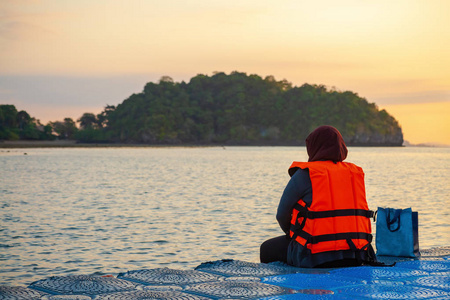 日出时分,一位身穿鲜橙色救生衣的妇女坐在浮桥码头上.