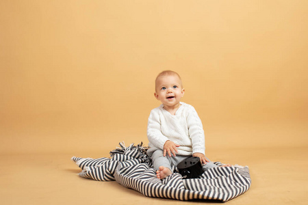 一个婴儿坐在灰色格子橙色背景上，手里拿着闹钟
