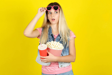 Young woman in sunglasses holding bucket with popcorn and paper 