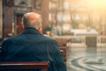 老人坐在教堂内的长凳上祈祷，后视图