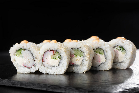 寿司卷内有虾，黄瓜和奶油芝士在黑石板隔离。加州卷覆盖白色芝麻。寿司菜单。水平照片。