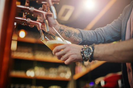 有纹身的高加索人，站在酒吧里倒啤酒。手上有选择地集中注意力。