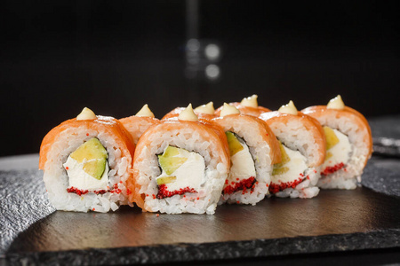 三文鱼卷鱼子酱寿司卷内有三文鱼,鳄梨,飞鱼鱼子酱和奶油芝士在黑色