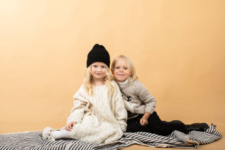 一个穿着白色针织连衣裙,戴着黑色帽子的小女孩和一个男孩坐在黄色