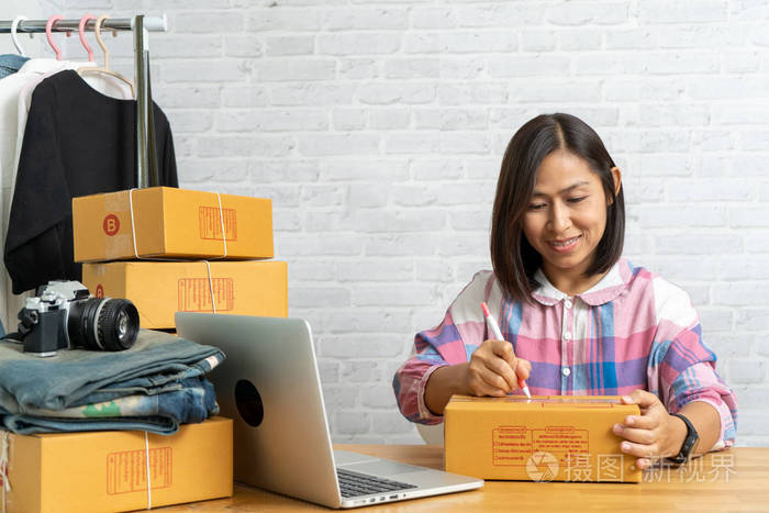 亚洲女性在线销售的创业小企业主工作，在家办公的邮包上写上地址