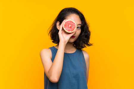 年轻的亚洲女孩拿着一个葡萄柚在孤立的橙色背景