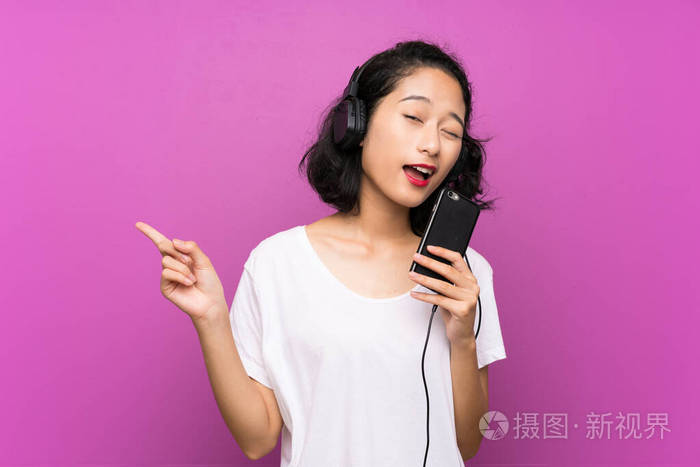 一个亚洲小女孩用手机听音乐在孤立的紫色墙上唱歌